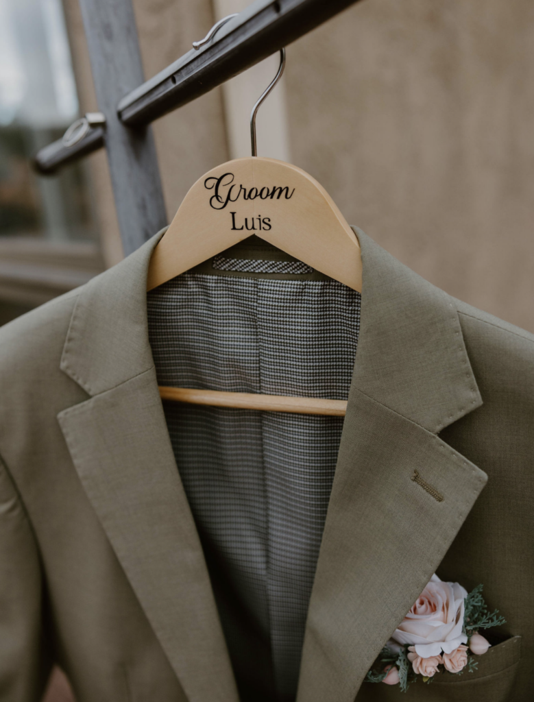 Grooms suit with boutonniere hanging on a customized hanger with his name on it 
